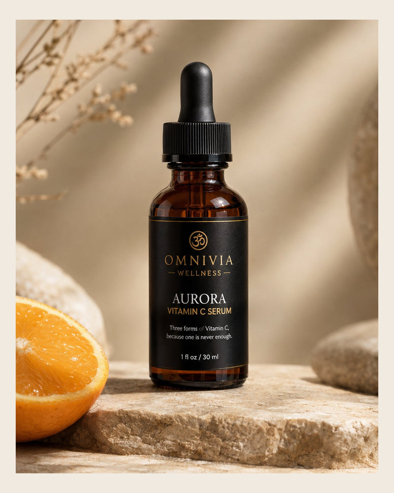Aurora Vitamin C Serum in an amber dropper bottle with a black and gold Omnivia Wellness label, beside a fresh orange half on stone