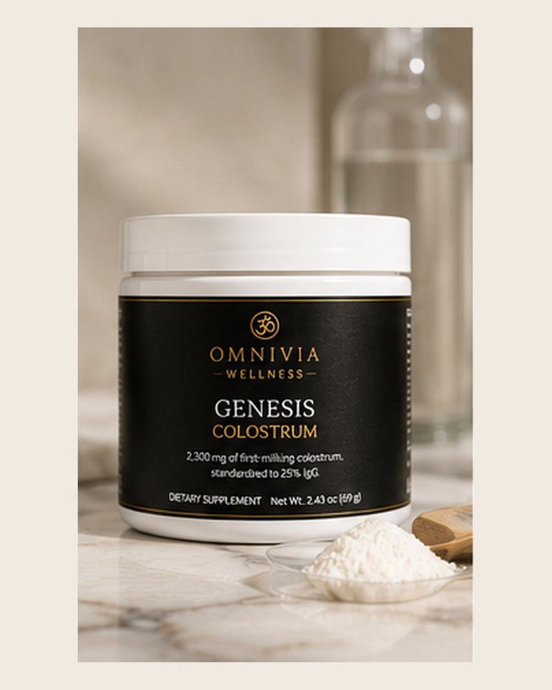 Genesis Colostrum jar with a black and gold Omnivia Wellness label beside a spoonful of colostrum powder on marble