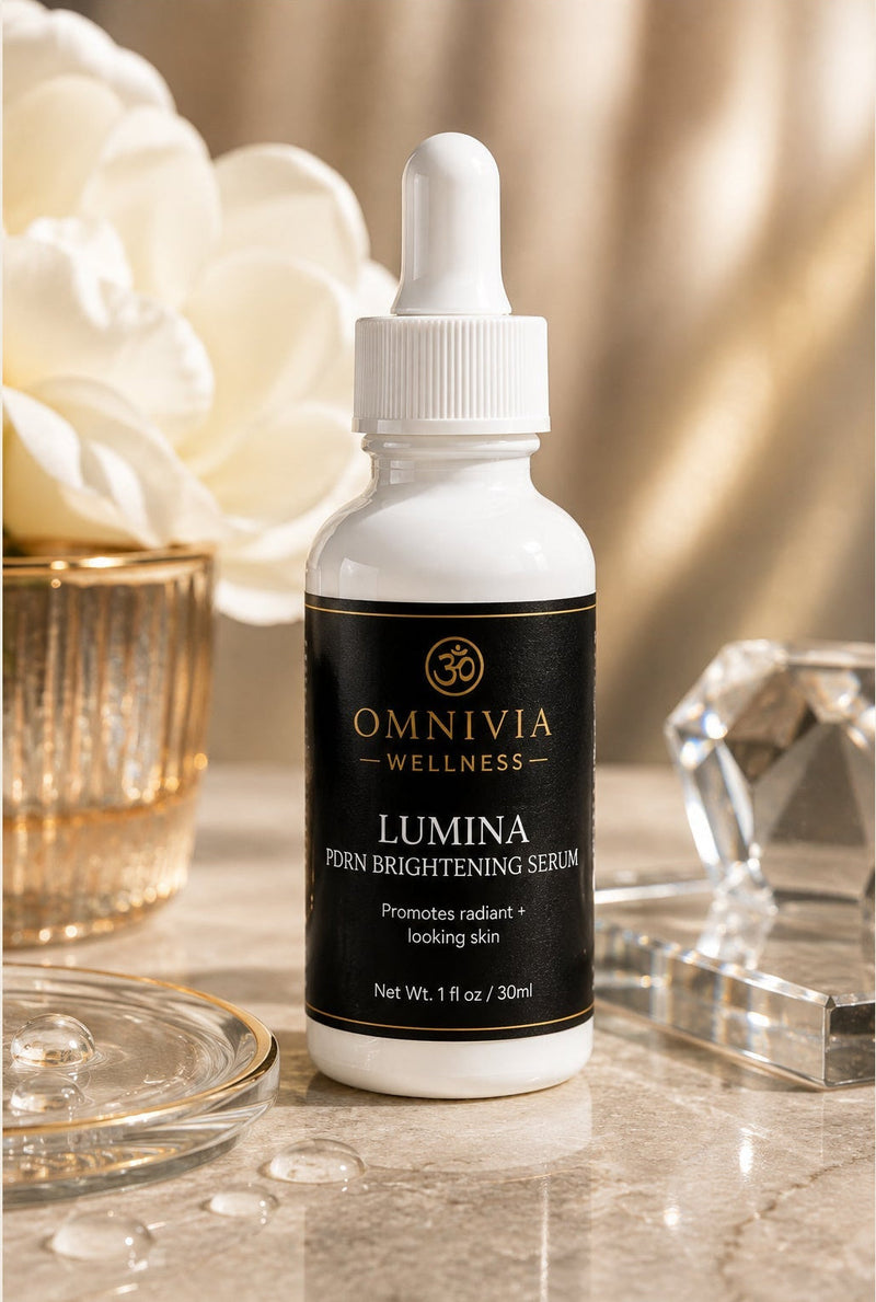 Lumina PDRN Brightening Serum in a white dropper bottle with a black and gold Omnivia Wellness label beside white flowers and crystal