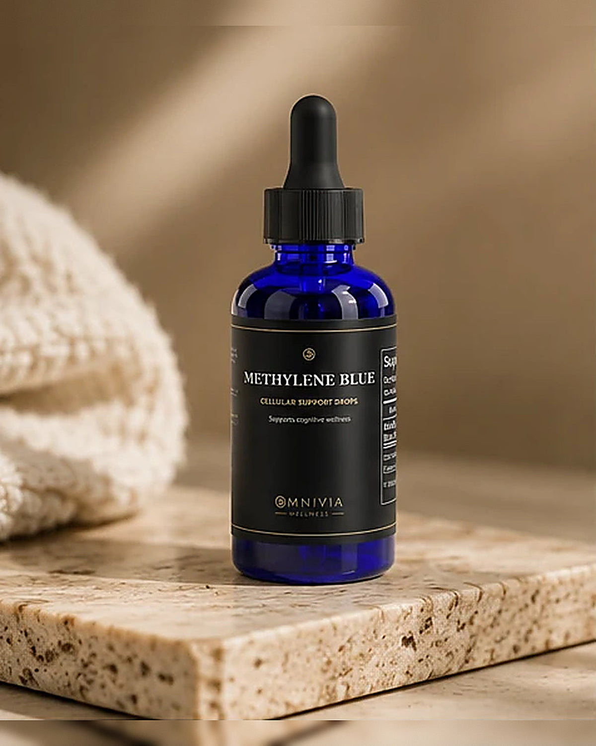 Omnivia Methylene Blue cobalt dropper bottle on a travertine slab beside a knit towel