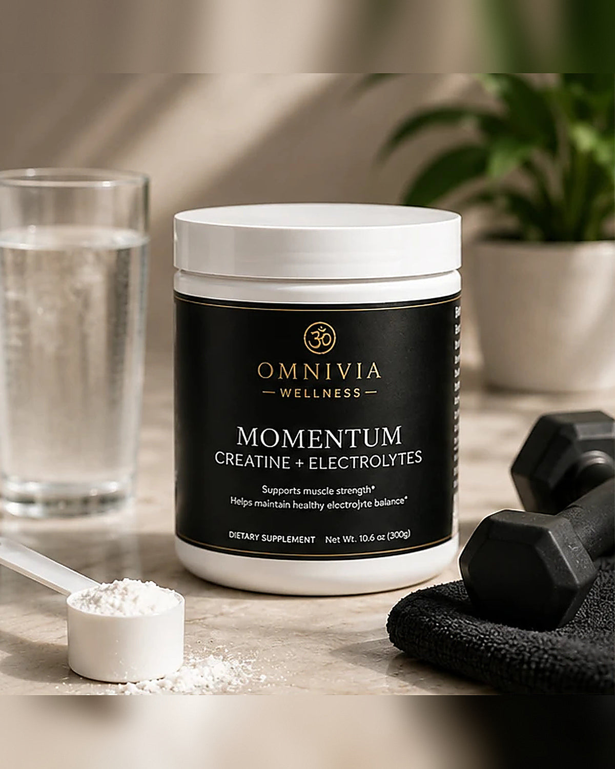 Momentum Creatine and Electrolytes tub with a scoop of powder, dumbbell, towel and a glass of water